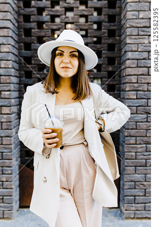 Portrait of successful business woman holding cup of cold drink in hand on her way to work on city street Portrait of successful business woman holding cup of cold drink in hand on her way to work on city street 125582395