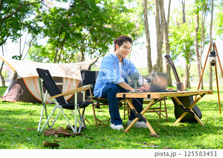 Young man using laptop at a table while camping in the forest 125583451