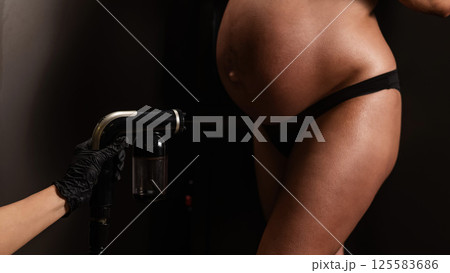 Close-up of the belly of a pregnant woman undergoing an instant tanning procedure. The master applies bronzer with a spray. Close-up of the belly of a pregnant woman undergoing an instant tanning procedure. The master applies bronzer with a spray. 125583686