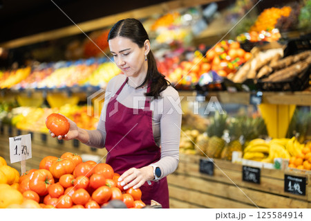 Middle-aged female seller putting tomatoes on counter in grocery market 125584914