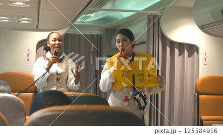 Asian stewardess safety explaining passengers prior to flight take off in airplane, air hostess uniform safety demonstration presenting pre-flight safety instructions life vest in emergency situation Asian stewardess safety explaining passengers prior to flight take off in airplane, air hostess uniform safety demonstration presenting pre-flight safety instructions life vest in emergency situation 125584916