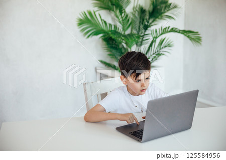 Boy studying at a desk with a laptop online 125584956