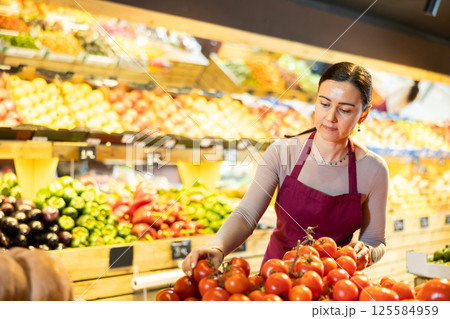 Supermarket employee carefully places ripe tomatoes on shelves of grocery supermarket Supermarket employee carefully places ripe tomatoes on shelves of grocery supermarket 125584959