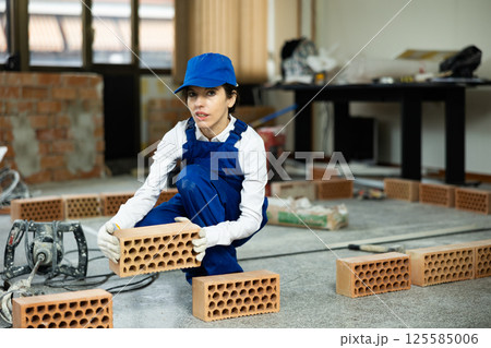 Woman builder stacks a wall of bricks in room Woman builder stacks a wall of bricks in room 125585006