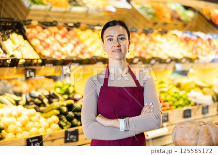 Middle-aged female seller standing by pumpkins in grocery market 125585172