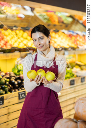Woman staff with apple in hands working in greengrocery 125585227