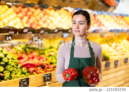 Middle-aged female seller offering red pepper in grocery market 125585230