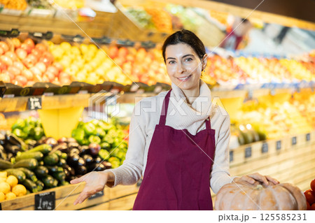 Young woman seller offering pumpkin in vegetable shop 125585231