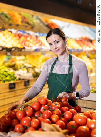 Supermarket employee carefully places ripe tomatoes on shelves of grocery supermarket 125585240