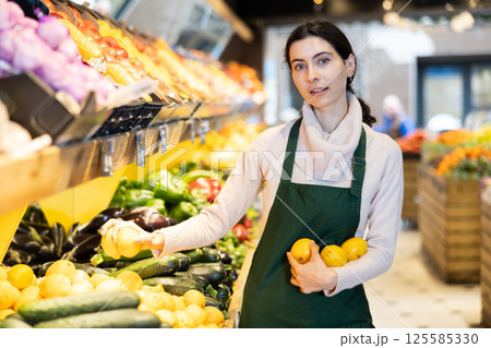 Woman staff with lemon in hands in greengrocery Woman staff with lemon in hands in greengrocery 125585330