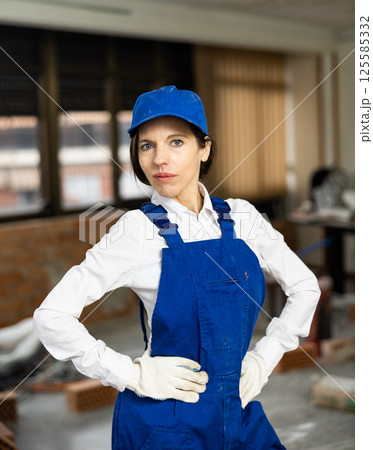 Woman foreman in blue overalls posing in house under construction 125585332