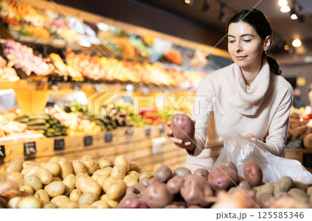 In vegetable store, young woman customer buy ripe potato In vegetable store, young woman customer buy ripe potato 125585346