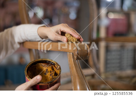 Close up of artisan hand applying wax to old vintage chair in furniture workshop 125585536