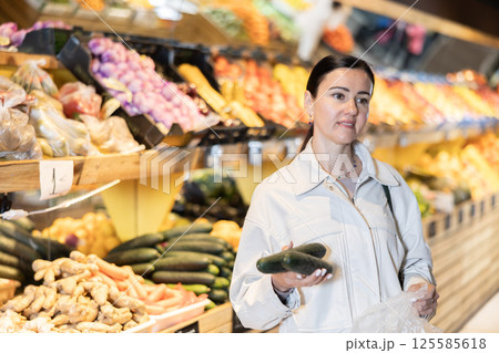 Middle-aged woman holding cucumbers in grocery store 125585618