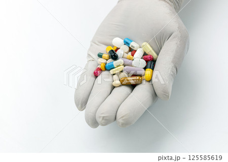 A close-up shot reveals a gloved hand delicately cradling a collection of pills. 125585619
