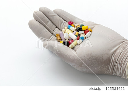 A gloved hand offers a kaleidoscope of pills, capsules, and tablets. 125585621