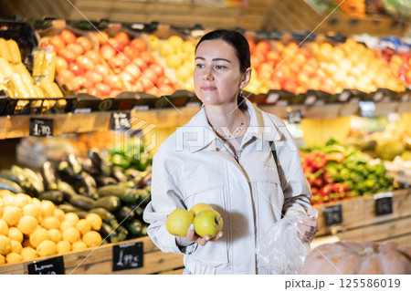 Portrait of female shopper carefully selecting ripe apples on supermarket display 125586019