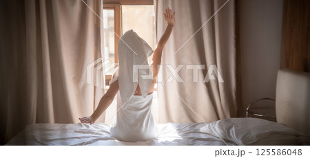Back view of young woman in towel sitting on bed and meditating Back view of young woman in towel sitting on bed and meditating 125586048