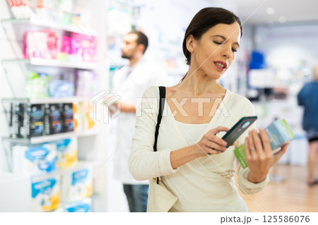 Woman choosing product using phone at pharmacy 125586076