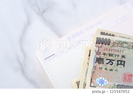 テーブルの上に開いた状態で置かれた銀行の預金通帳と、1万円札 テーブルの上に開いた状態で置かれた銀行の預金通帳と、1万円札 125587052