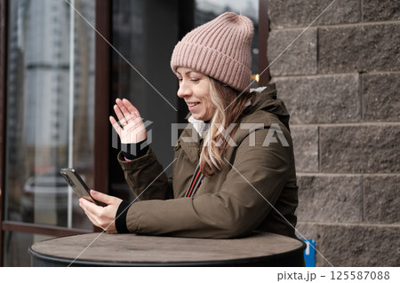 Portrait of mature woman in wool hat standing on the urban street, drinking takeaway coffee from paper cup. Middle-aged 40s female walking around the city at cold autumn day. Living in modern district Portrait of mature woman in wool hat standing on the urban street, drinking takeaway coffee from paper cup. Middle-aged 40s female walking around the city at cold autumn day. Living in modern district 125587088