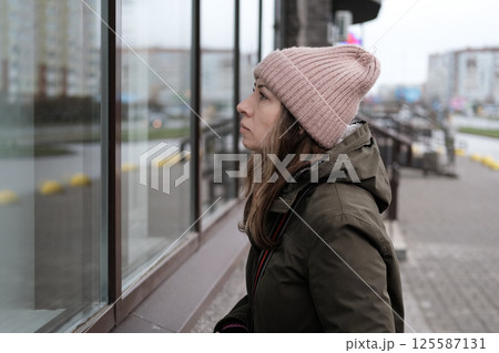 Portrait of mature woman in wool hat standing on the urban street, drinking takeaway coffee from paper cup. Middle-aged 40s female walking around the city at cold autumn day. Living in modern district 125587131