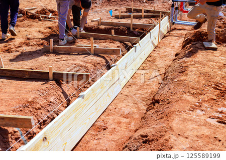 Workers are setting up wooden forms for foundation in construction area during work day 125589199
