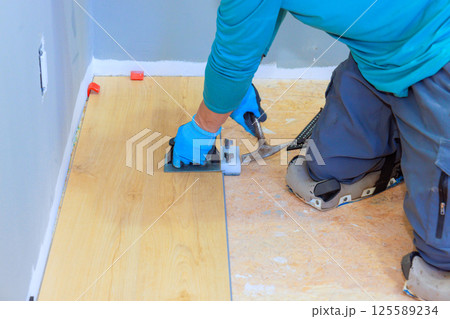 Worker laying vinyl laminate flooring planks while kneeling on plywood in house renovation Worker laying vinyl laminate flooring planks while kneeling on plywood in house renovation 125589234