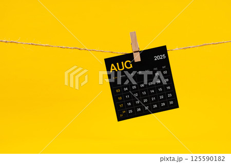 August 2025 black calendar hanged with brown rope on yellow. 125590182