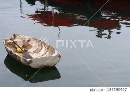 a weathered aged rowboat floating gently on calm water, cracked and peeling paint, with reflection on the water. There is copyspace. a weathered aged rowboat floating gently on calm water, cracked and peeling paint, with reflection on the water. There is copyspace. 125590467