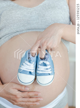 Tender Pregnancy Moment: Baby Shoes Resting on Expectant Mother's Belly Tender Pregnancy Moment: Baby Shoes Resting on Expectant Mother's Belly 125591215