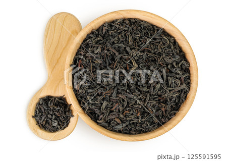 Dry black tea leaves in wooden bowl and spoon isolated on white background. Top view. Flat lay 125591595
