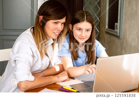 Daughter showing mom something exciting on internet on laptop screen sitting at table in kitchen. Happy parenthood and motherhood. Happy family concept. Daughter showing mom something exciting on internet on laptop screen sitting at table in kitchen. Happy parenthood and motherhood. Happy family concept. 125591838