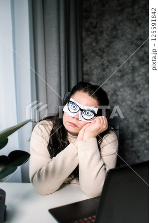 Tired business woman with painted eyes on adhesive notes having fatigue and headache during work in office. Female feeling stressed and exhausted from overworking Tired business woman with painted eyes on adhesive notes having fatigue and headache during work in office. Female feeling stressed and exhausted from overworking 125591842