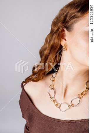 closeup of woman wearing abstract chain necklace and gold earrings, jewelry on exposed collarbones and bare shoulders with red wavy hair, accessories brand, jewelry design, luxury fashion closeup of woman wearing abstract chain necklace and gold earrings, jewelry on exposed collarbones and bare shoulders with red wavy hair, accessories brand, jewelry design, luxury fashion 125591954