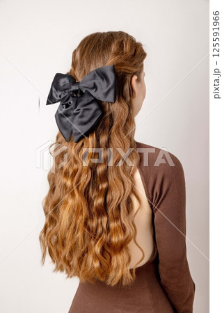 young woman with long wavy red hair styled with large black bow accessory, side rear view in minimalist bright studio with neutral background, hair fashion, beauty salon, hair accessories young woman with long wavy red hair styled with large black bow accessory, side rear view in minimalist bright studio with neutral background, hair fashion, beauty salon, hair accessories 125591966