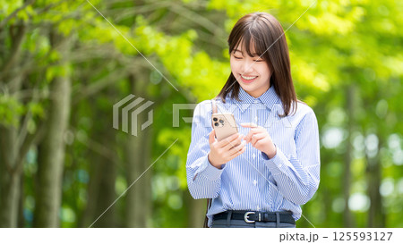 遊歩道でスマートフォンを使う笑顔の女性・ビジネスウーマン 遊歩道でスマートフォンを使う笑顔の女性・ビジネスウーマン 125593127