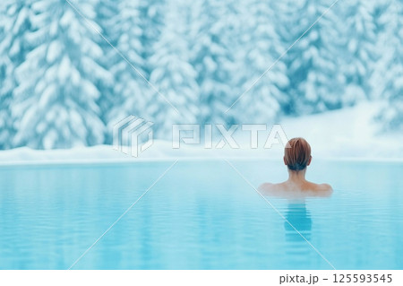Woman enjoys tranquility in hot spring surrounded by snow-covered trees under soft morning light 125593545