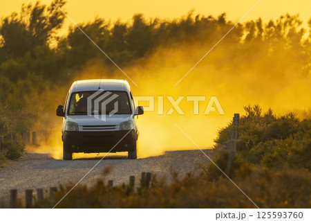 White van driving on dusty road at sunset 125593760