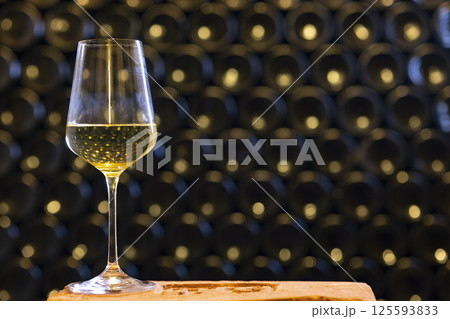 Glass of white wine resting on a brick in a wine cellar 125593833