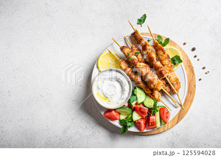Grilled chicken kebabs with fresh vegetable salad and tzatziki sauce 125594028