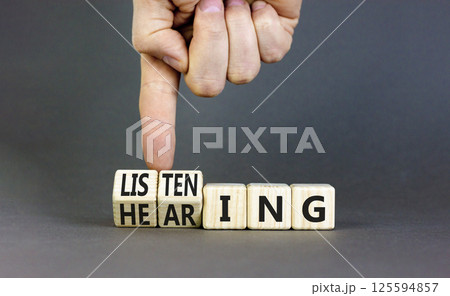 Listening or hearing symbol. Businessman turns wooden cubes and changes a concept word Listening to Hearing. Beautiful grey background. Copy space. Business educational listening or hearing concept. 125594857