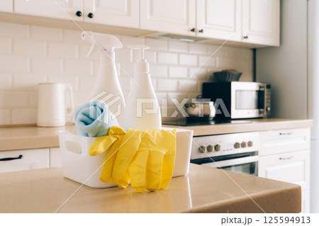 Kitchen cleaning supplies on countertop with gloves and spray bottles in modern white interior 125594913
