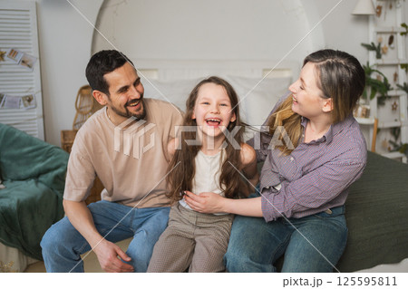 Happy family at home. Mother father children daughter relaxing on sofa indoor. Mom dad parents kid girl relax playing hugging having fun together. Family smiling laughing enjoying tender moment 125595811