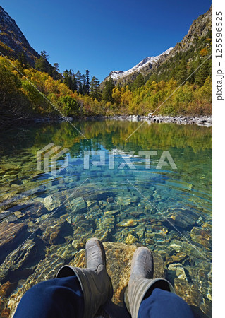 Legs of a tourist in boots against the background of a mountain lake with an autumn forest 125596525