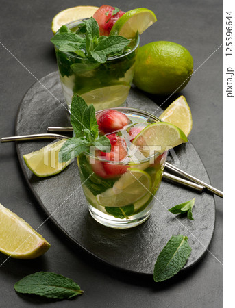 Refreshing mojito cocktail with lime, mint, strawberry, and ice on dark background Refreshing mojito cocktail with lime, mint, strawberry, and ice on dark background 125596644