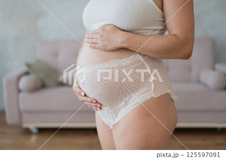 Caucasian pregnant woman in adult diapers suffers from incontinence. Close-up of belly.  125597091