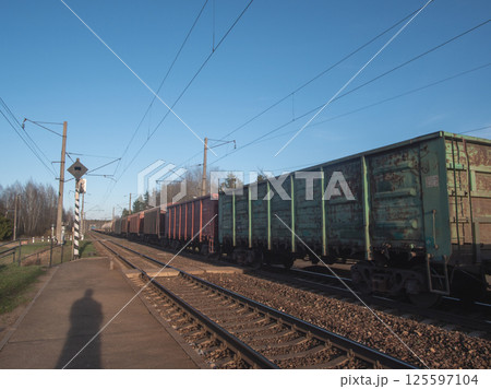 A freight train waits at a busy station under a clear blue sky, perfect for transport themes and narratives A freight train waits at a busy station under a clear blue sky, perfect for transport themes and narratives 125597104