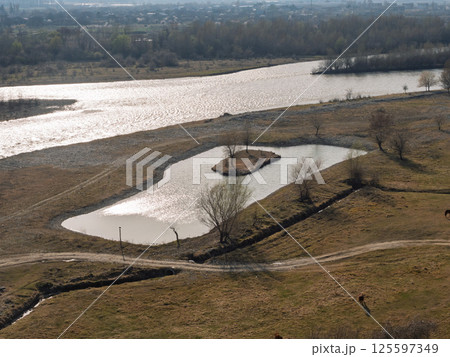 Aerial view of a small artificial lake reflecting sunlight near kura river in georgia, surrounded by dry grassland 125597349