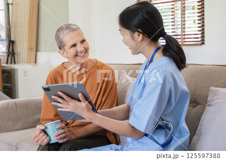 Young Nurse Providing Health Care Advice to Elderly Woman in a Comfortable Home Setting with Digital Tablet and Warm Smiles 125597388